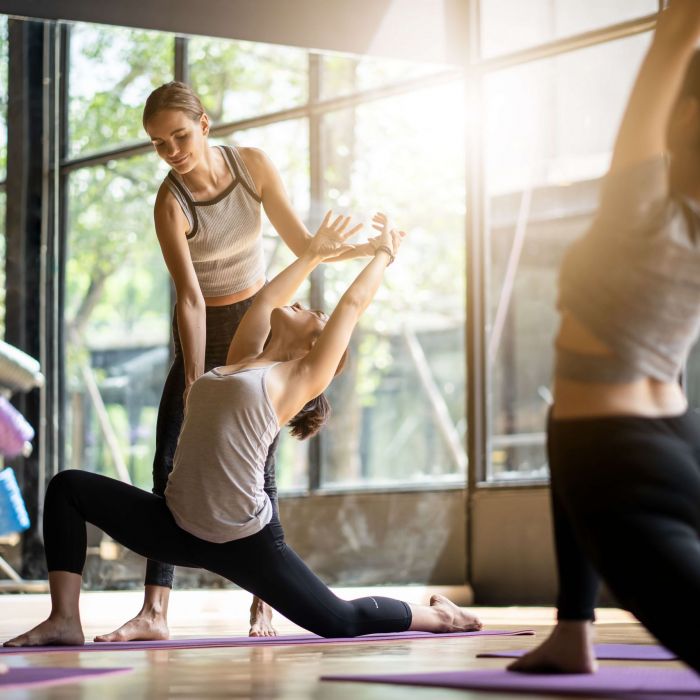 Trainerin gibt einer Besucherin eines Fitnessstudios eine Hilfestellung bei einer Übung